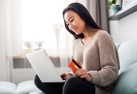 Imagem da campanha de varejo mostrando uma mulher em seu sofá com um cartão de crédito e um laptop
